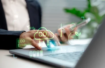 Frauenhand mit Laptop, darüber liegen Icons, die die CO2-Reduktion symbolisieren